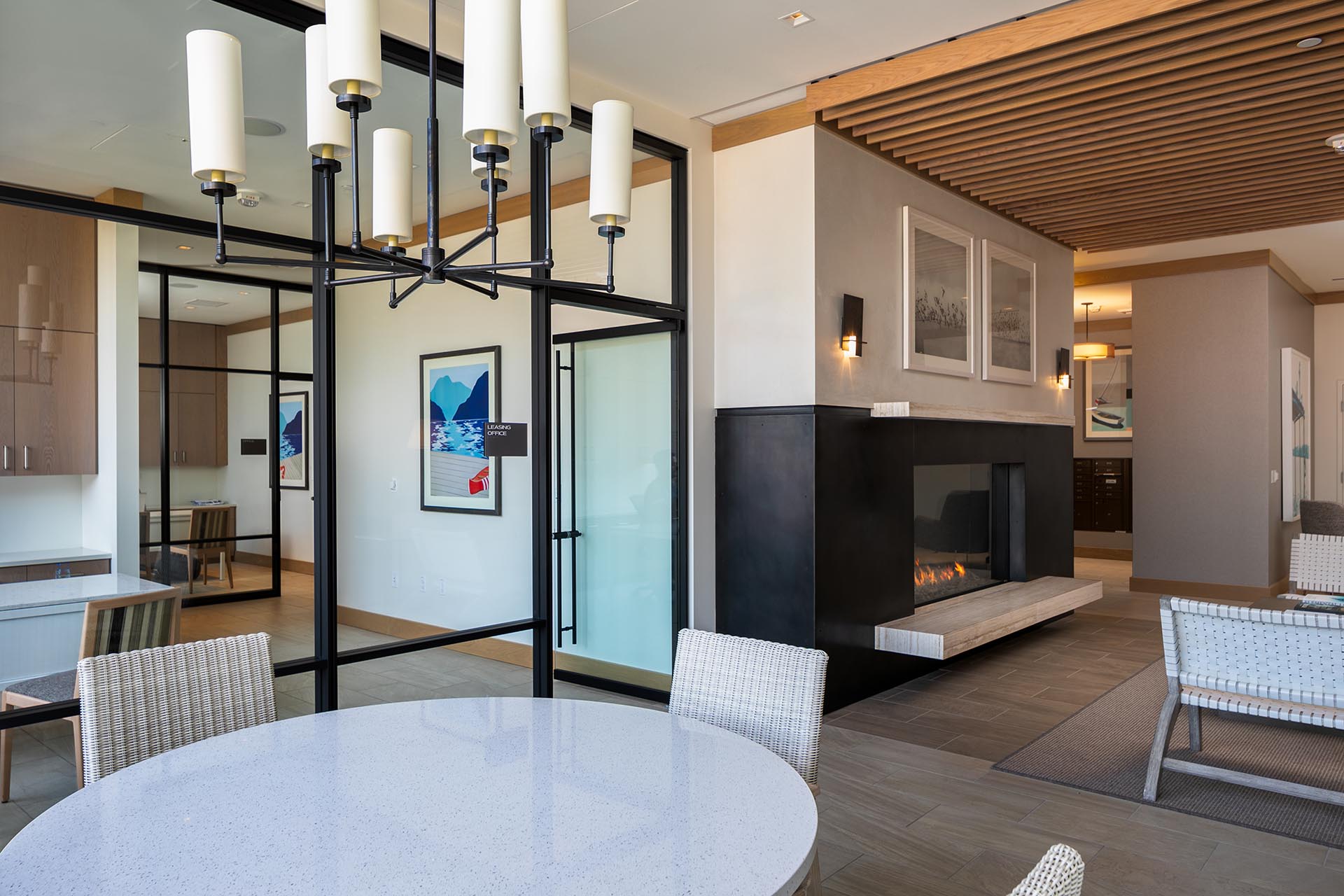 Several rooms, separated by glass walls and a large modern fireplace with a marble ledge