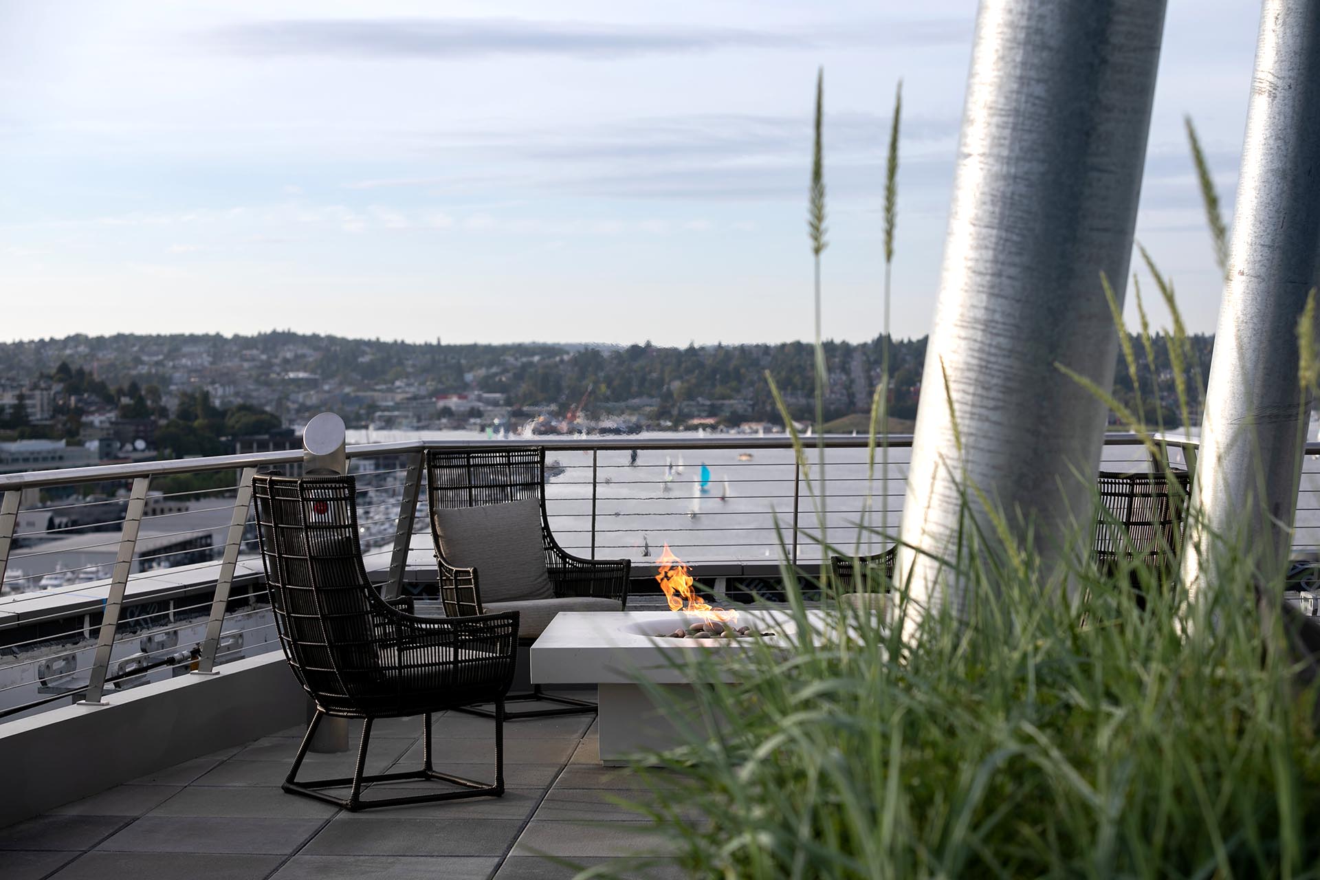 A small mounted firepit on the deck, encircled by outdoor seating, and the city/lake in the background